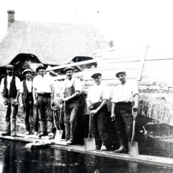 Workmen on a plank across the river Test, adjacent the road bridge opposite Vine Cottage, Fullerton | Bill Pickett